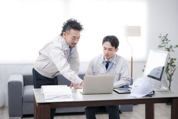 Fototapeta premium パソコンを見ながら話す作業着のビジネスマン2人 製造業などのdxやit化、見積もりイメージ