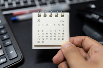 Hand holding MARCH 2026 calendar with calculator for financial stress and budget crisis concept. financial anxiety, calculating monthly expenses, debt management.