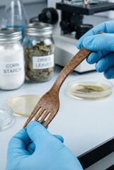 Scientist in lab inspecting biodegradable fork made from plant fibers, sustainable material research