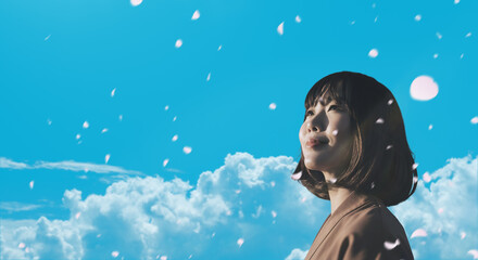 春・上を見上げ微笑む明るい表情の日本人女性の顔　前向きでポジティブ希望に満ちた表情　就職・新生活・新入社員,旅行・リラックス・入学のイメージ　青空と雲の背景 風に舞い散る桜の花びら