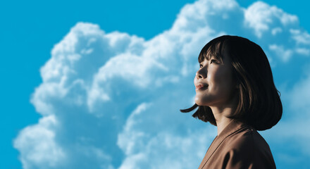 春・上を見上げ微笑む明るい表情の日本人女性の顔　前向きでポジティブ希望に満ちた表情　就職・新生活・旅行・リラックス・入学のイメージ　青空と雲の背景