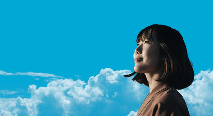 春・上を見上げ微笑む明るい表情の日本人女性の顔　前向きでポジティブ希望に満ちた表情　就職・新生活・旅行・リラックス・入学のイメージ　青空と雲の背景