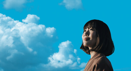 春・上を見上げ微笑む明るい表情の日本人女性の顔　前向きでポジティブ希望に満ちた表情　就職・新生活・旅行・リラックス・入学のイメージ　青空と雲の背景