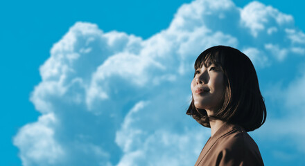 春・上を見上げ微笑む明るい表情の日本人女性の顔　前向きでポジティブ希望に満ちた表情　就職・新生活・旅行・リラックス・入学のイメージ　青空と雲の背景