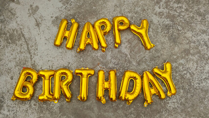 Golden Metallic Happy Birthday Foil Alphabet Balloons Laid Out on a Textured Grey Concrete Ground for an Urban Celebration Concept