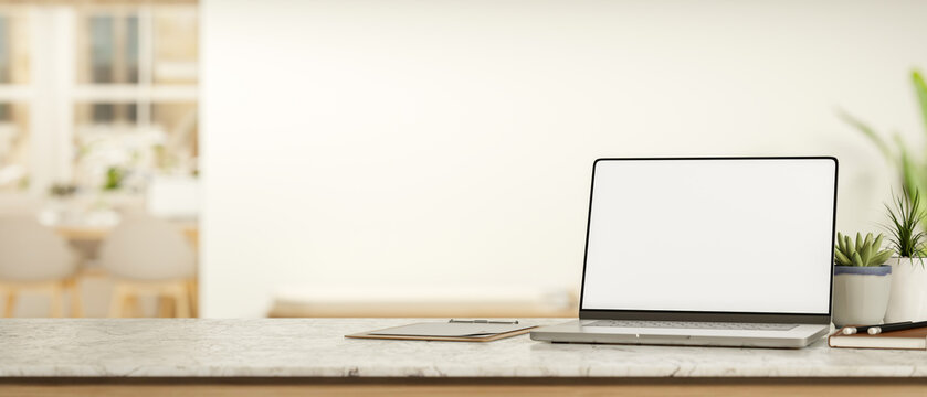White screen laptop with book and clipboard on marble counter table across white wall in living room