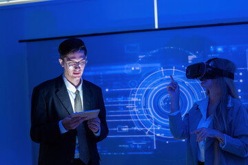 Person wearing virtual reality headset interacts with technology while another person analyzes data in a modern workspace