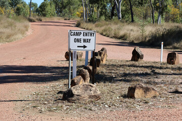 Camp Entry One Way sign next to a gravel road with rocks and trees
