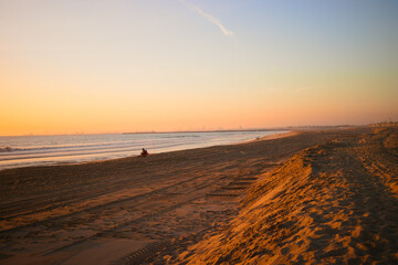 Obraz premium Golden sunset light washes over the shoreline and sand dunes at Sunset Beach, California, with calm waves, long shadows, and a peaceful coastal scene.