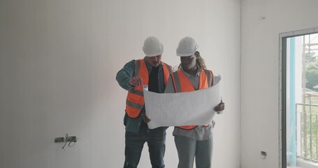 Engineer discuss blueprint at construction site, making decisions for architectural plan on upper floor. Both are dressed in safety gear. Collaborative approach to ensure project accuracy and progress