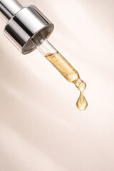 Close-up of a glass dropper dispensing a golden liquid drop, highlighting skincare or scientific application.