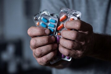 Closeup of male hands tightly clutching multiple blister packs of colorful medication pills