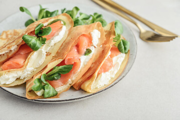 Crepes or thin pancakes with lightly salted salmon, soft cheese and cornsalad
