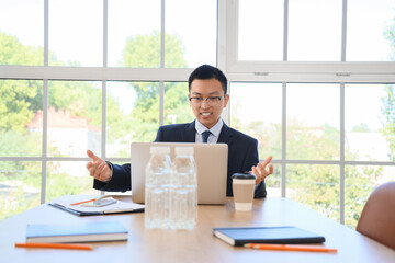 Fototapeta premium Chinese businessman with laptop video chatting at table in office