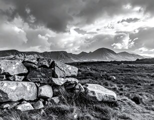 Black and white landscape featuring a weathered stone wall in the foreground. Rolling hills stretch into the distance under a dramatic, cloudy sky