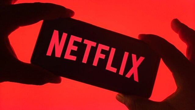 Hands holding smartphone displaying the netflix logo against a vibrant red background