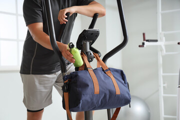 Man taking water bottle from sports bag on elliptical machine at gym