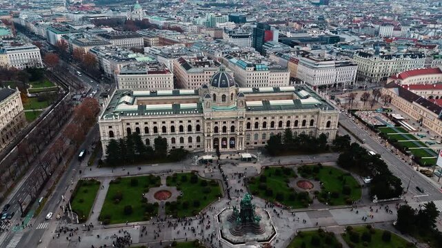 Aerial drone shot panning left over the Austrian History Museum in Vienna, showing the historic building and surrounding streets, with the Vienna cityscape visible in the background under clear skies