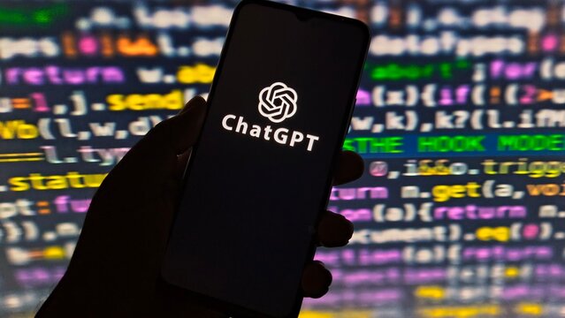 Hand holding smartphone displaying chatgpt logo against a background of colorful programming code