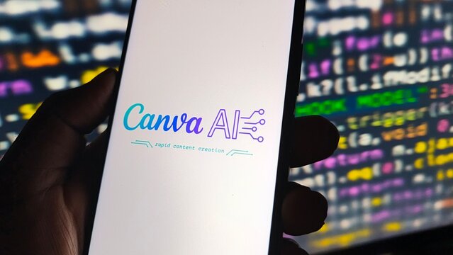 Closeup of canva ai logo displayed on a smartphone screen held by a hand, with code in the background