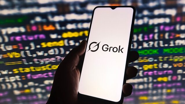 Hand holding smartphone displaying grok ai logo against a background of programming code