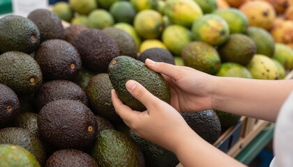 Hands selecting a ripe Hass avocado from a piled produce display at a market or supermarket