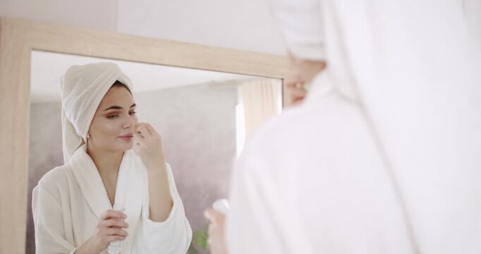 Slow motion of woman with beautiful face and perfect skin just cleaned from impurities pampering. Make-up preparation. Woman applying skin care cream on her face to make face soft and fresh