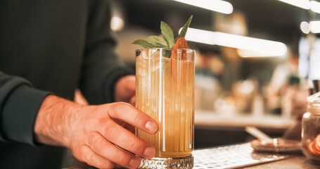 Cold drink. Served cocktail. Bartender hand offering tall glass of juice ice cubes with aromatic sprig green mint dried orange slice.