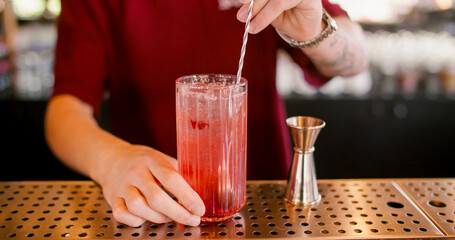 Stirring drink. Cocktail recipe. Bartender mixing flavored refreshing beverage with long metal spoon. Professional metal jigger for measuring.