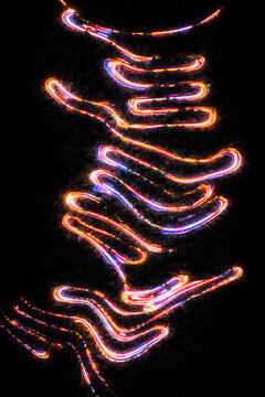Aerial night view of a road in Trichy city kolli hills though dark forest, captured in long exposure, with vibrant neon light trails forming glowing, serpentine patterns against the black landscape.