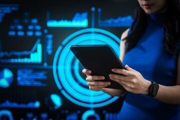 Woman holding tablet computer with futuristic blue data dashboard background, digital analytics, smart technology, data visualization, business intelligence, advanced user interface design.