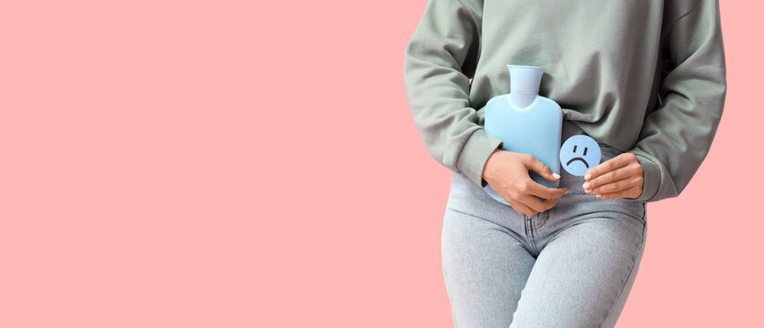 Young woman with sad emoticon and hot water bag on pink background, closeup. Cystitis concept