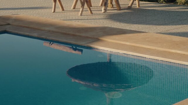 Tranquil poolside scene in Morocco with rustic wooden furniture and a clear blue pool reflecting the sky. The serene atmosphere invites relaxation and escape, essence of a peaceful holiday.