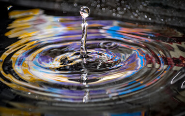 macro capture of a water droplet rising from a narrow column, forming concentric ripples on a dark, reflective surface. Ideal for science, nature, and beautiful visuals