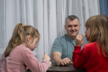 Fototapeta premium Smiling man enjoys dessert with two young girls in a cozy indoor setting during the evening