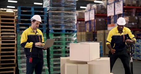 Caucasian male warehouse supervisor wearing hardhat using digital tablet for inventory inspection near stacked cardboard boxes and wooden pallets inside modern logistic storage facility - Powered by Adobe