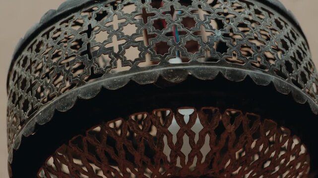 Close-up of an intricate Moroccan lamp, its metal latticework casting decorative shadows. The light filters through geometric patterns, The lamp's aged texture adds to its charm,