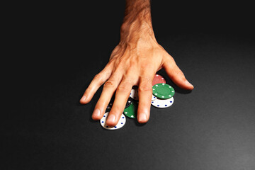 Man's hand holding green and red poker chips on a black background
