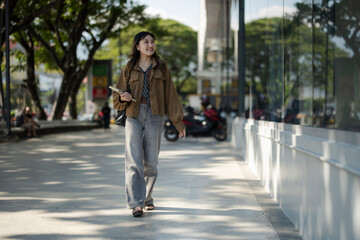 Young asian woman walking street smiling holding book