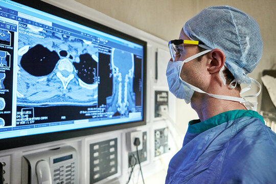 Surgeon, man and review CT scan in hospital for surgery planning, tumor progress and assessment. Medical scrubs, doctor and screen with digital imaging in theater for biopsy procedure and operation