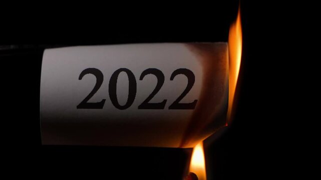 White sheet of paper with the number 2022 being set on fire in slow motion, close-up on black background