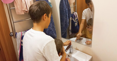 Boy helping younger sibling brush teeth in bathroom mirror  