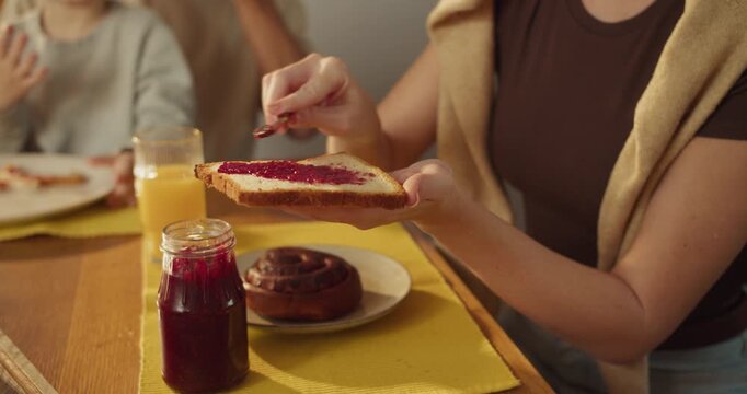 Caucasian mother prepping toast with berry jam for breakfast