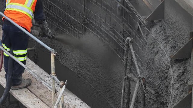 Construction worker on a construction site with scaffolding shooting shotcrete concrete from a nozzle onto steel rebar.