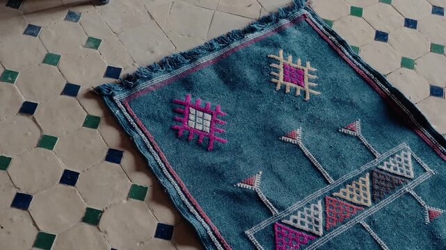 A vibrant blue Moroccan rug with colorful, traditional Berber patterns lies on a tiled floor. The geometric designs and fringed edges showcase the artistry of Moroccan craftsmanship. culture,