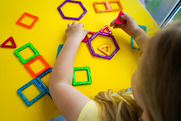 A child explores geometry through play, connecting colorful magnetic shapes to create balanced and imaginative three-dimensional forms.