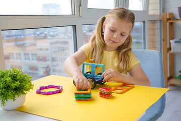 A child's hands carefully connect magnetic construction pieces against a sunny yellow background, demonstrating the joy of educational and creative playtime