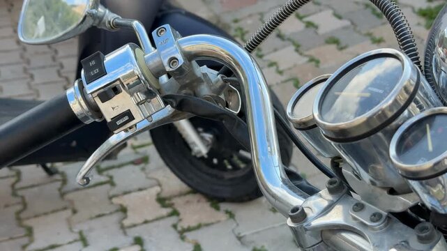 Motorcycle handlebar and gauges with chrome details, parked on stone pavement background