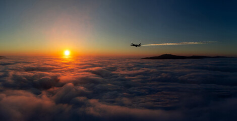 A scenic moment of an airplane flying above the clouds during sunset