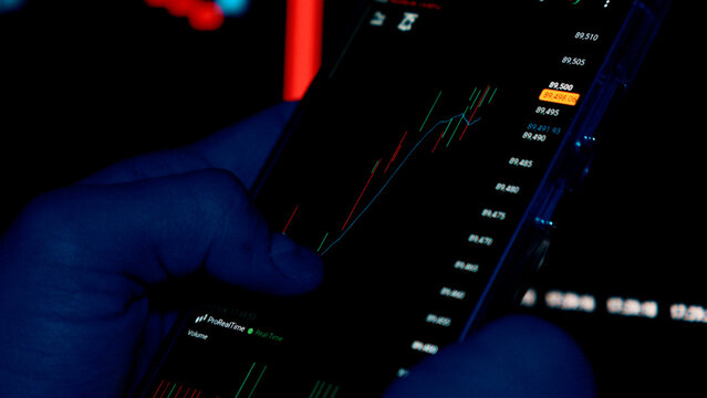 Hands in blue gloves holding smartphone with stock market charts. - Powered by Adobe